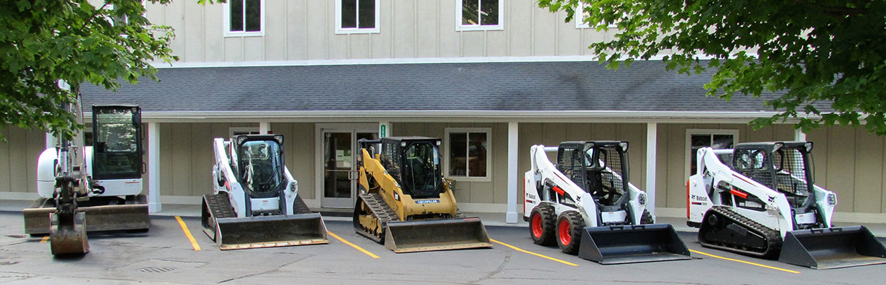 4 Skid steers and a mini excavator in front of the Woodhams Equipment